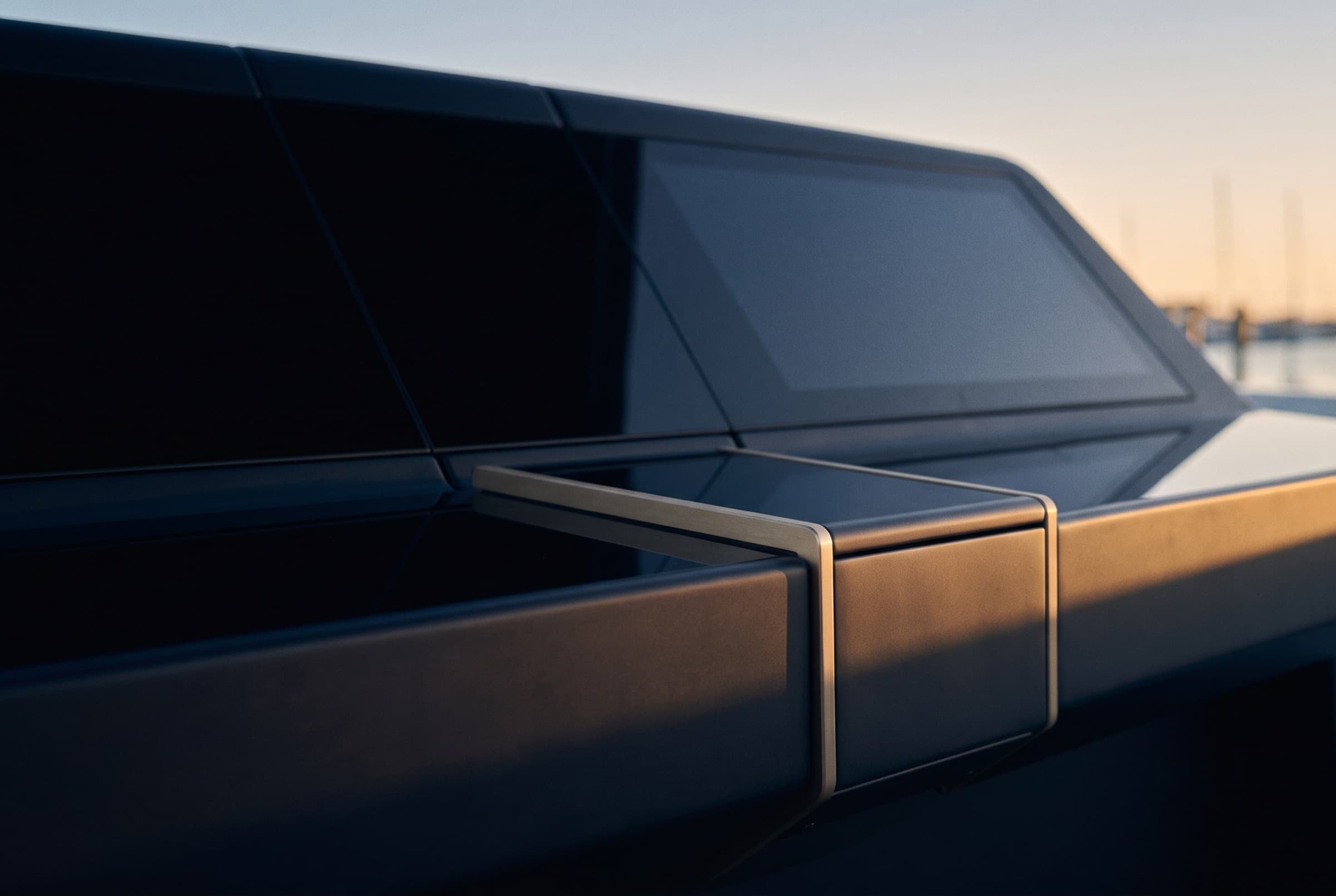 A dark, minimal console at rest at dusk; flush screens unlit, a single warm metal edge catching the light.