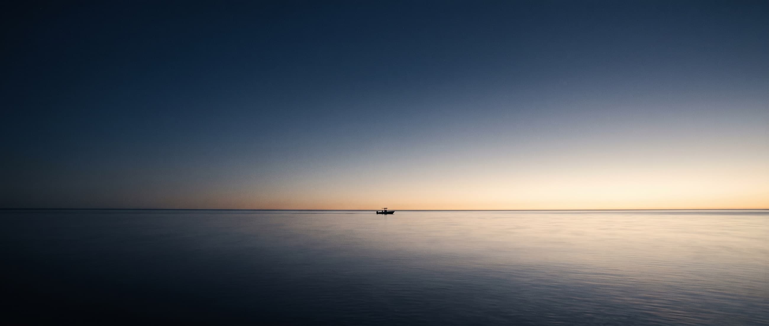 A single center console far on a calm horizon at dusk, almost lost in open water.